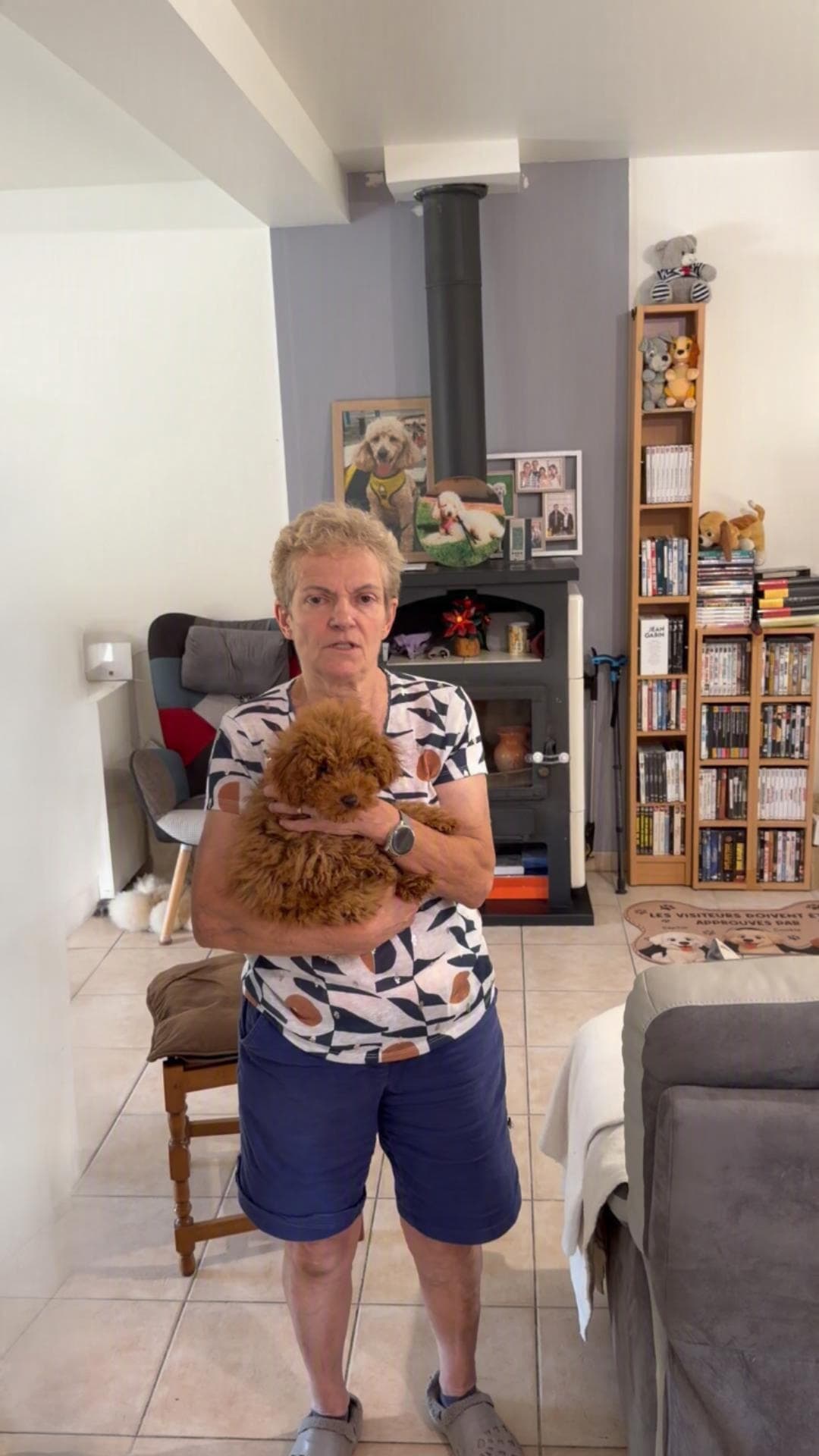 Une aidante tenant un jeune chien caniche dans les bras, dans un salon