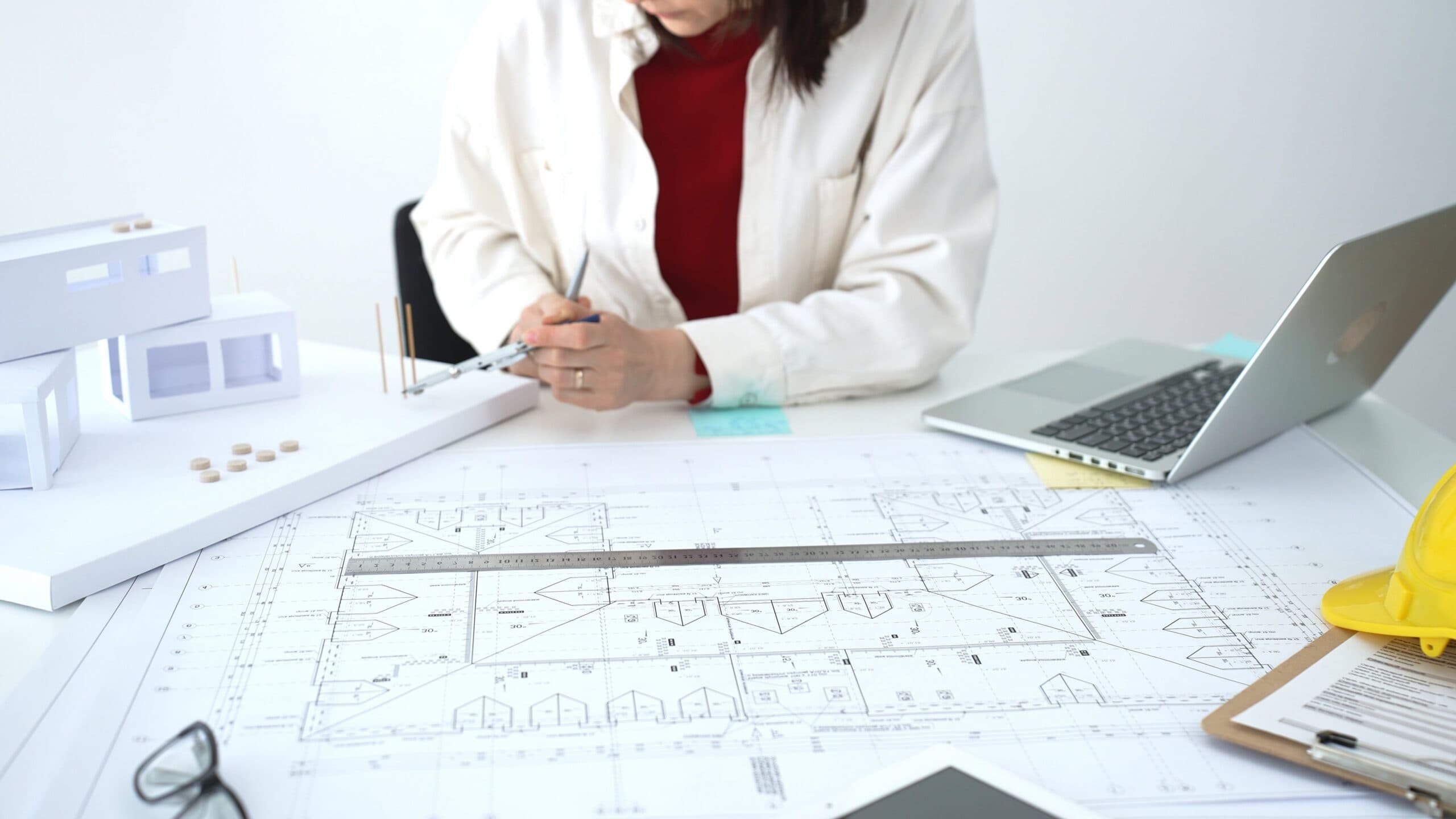 Architecte dessinant des plans de construction sur un bureau, avec maquette et casque de chantier