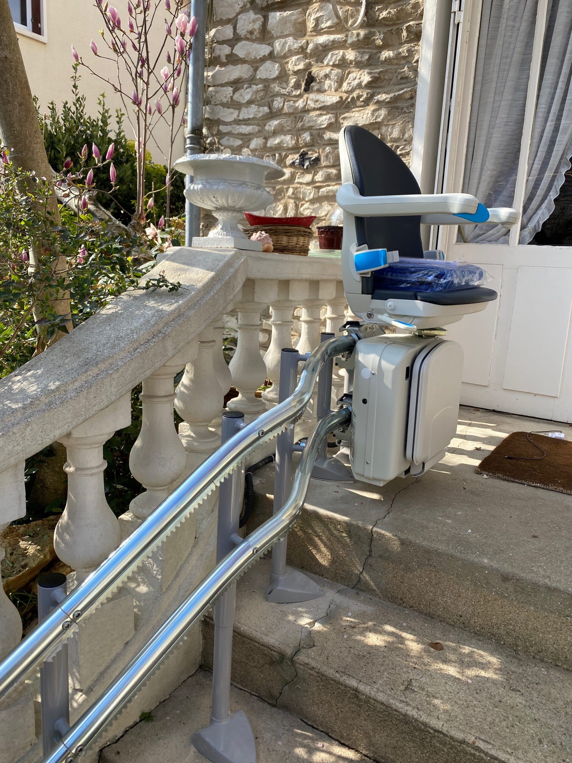 Monte-escalier extérieur avec siège replié, installé sur un escalier en pierre avec balustrade