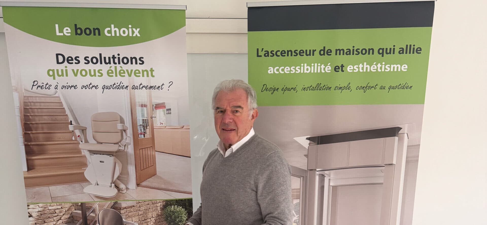 Un homme dans un showroom, entouré de banderoles présentant des monte-escaliers et un ascenseur de maison